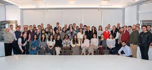 Large group of professionals pose together for a team photo in a bright modern office space.