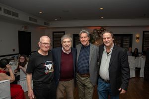 Four men smiling and posing together at a casual dinner event inside a warmly lit restaurant venue.