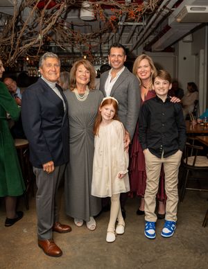 Multi-generational family of six posing together at an elegant indoor celebration with decorative branch centerpieces.