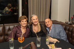 Three guests smiling together at a dimly lit restaurant booth with cocktails.