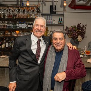 Two older men smiling together in front of a stylish restaurant bar.