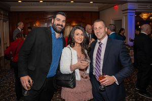 Three guests smile together holding cocktails at an elegant indoor reception.