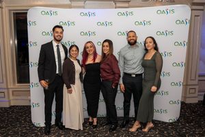 Five young professionals posing together in front of an Oasis branded step-and-repeat banner at a formal event.
