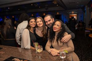 Group of four friends smiling and posing together at a lively bar event with cocktails on the counter.