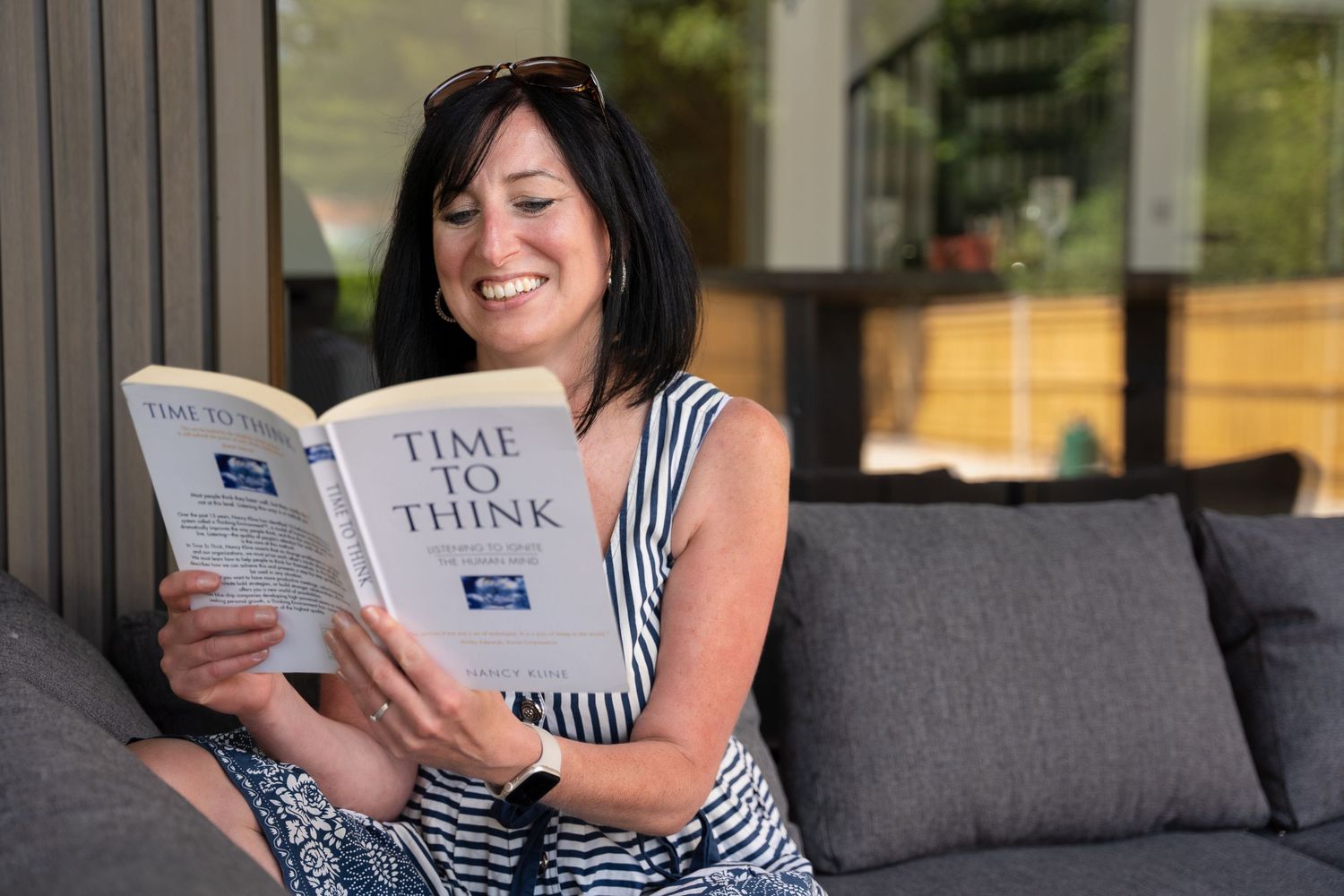 Life coach reads a book, smiling on a sofa, during her personal branding photo shoot in Fareham.