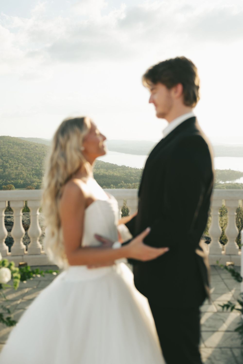 Bride and groom sharing a romantic moment on a balcony with scenic water views.