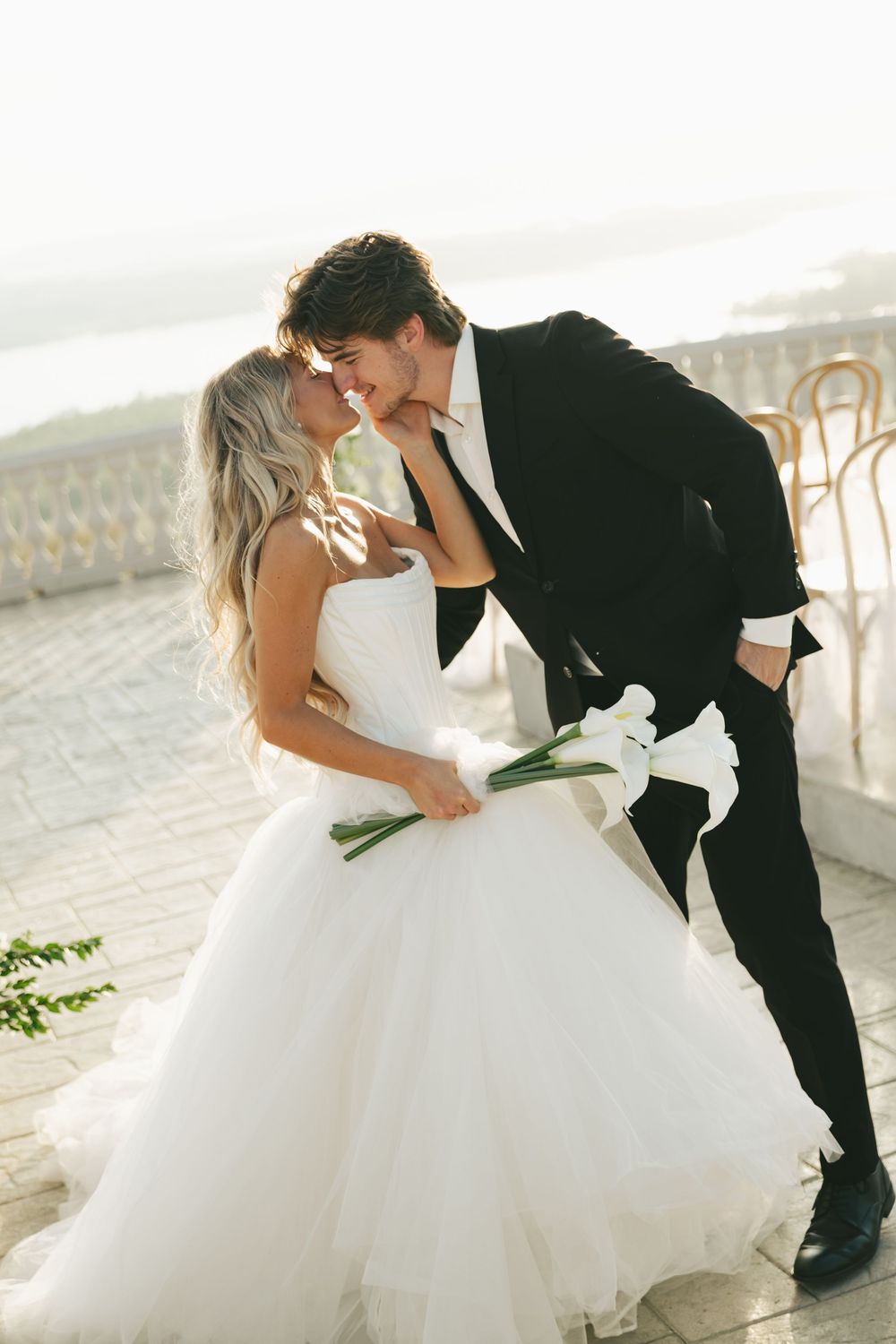 Bride and groom sharing an intimate moment, nearly kissing, bride holding white calla lily bouquet in elegant white ballgown.