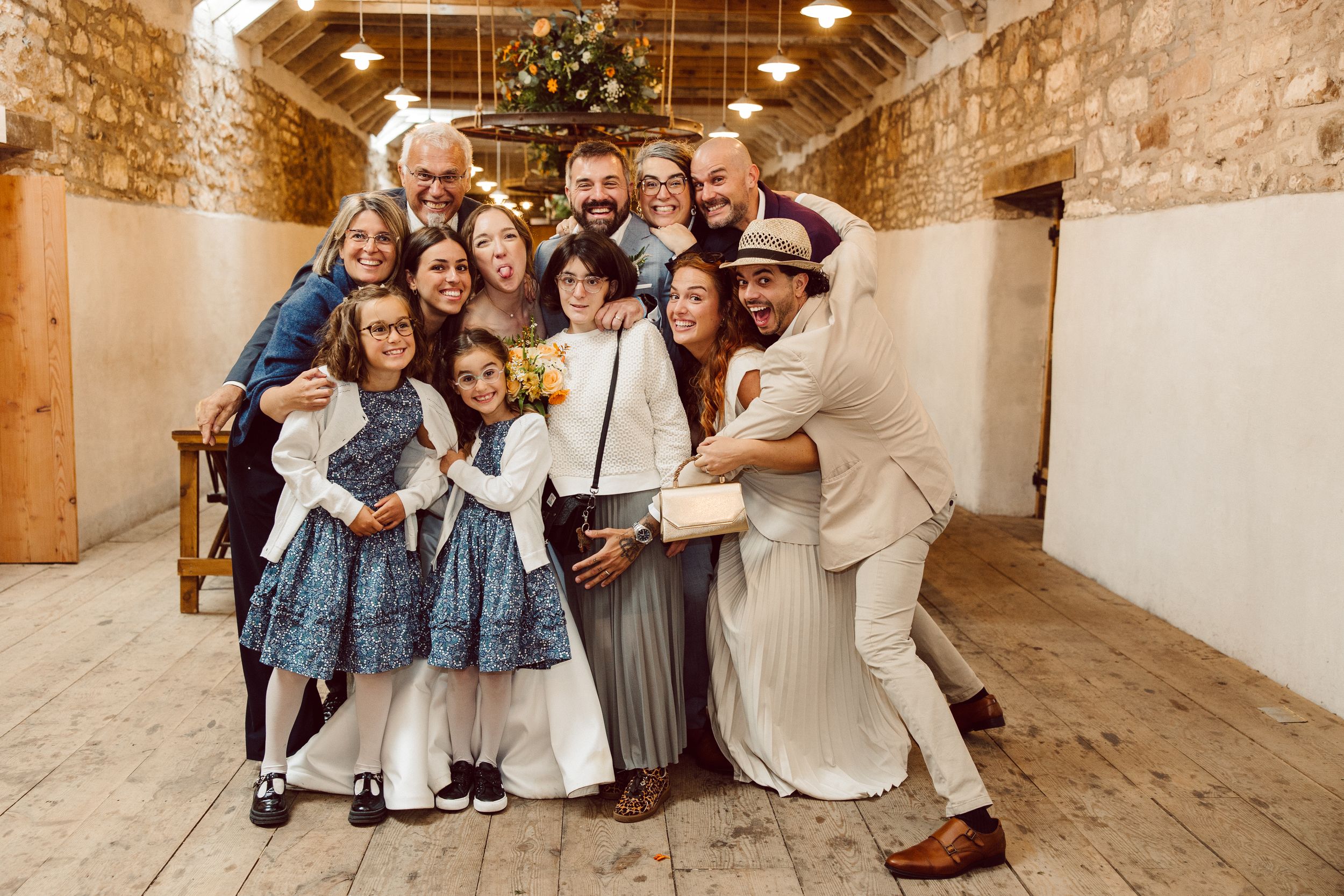 A joyful group poses together at a rustic barn wedding venue with exposed stone walls and wooden beams.