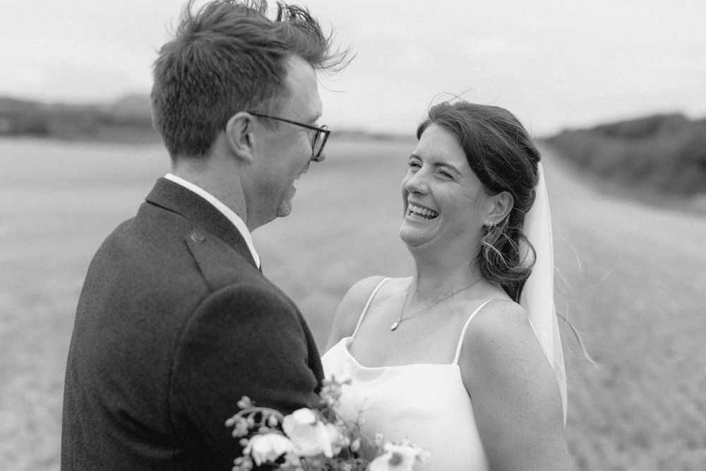 Black and white candid photo of a joyful couple sharing a happy moment on their wedding day in an outdoor setting.