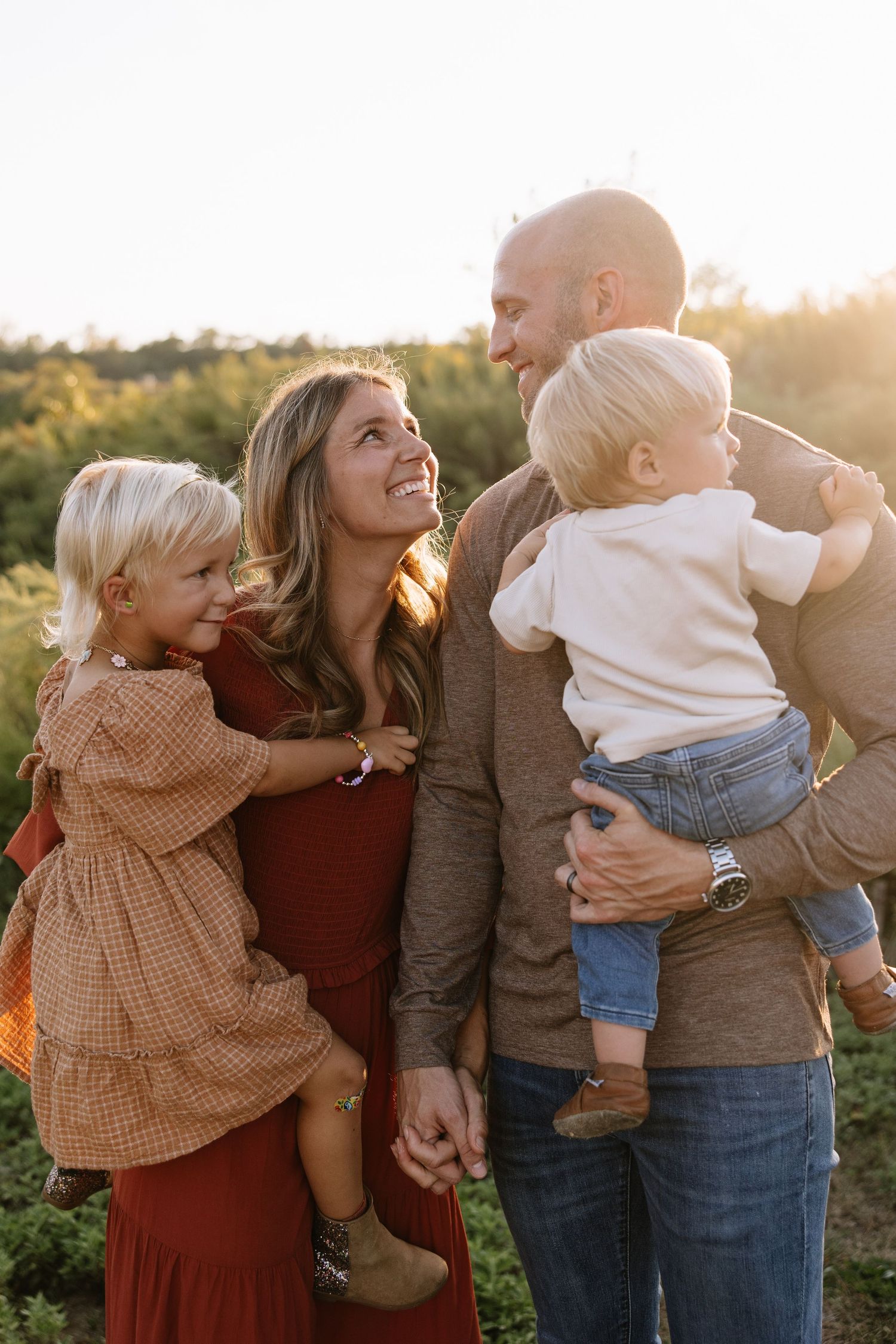 A family embraces and laughs together during a sunset photoshoot in an outdoor field.