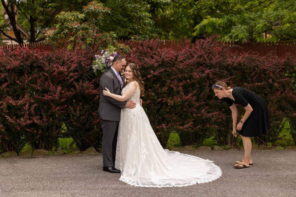 A wedding party poses in front of red flowering bushes in an outdoor garden setting.