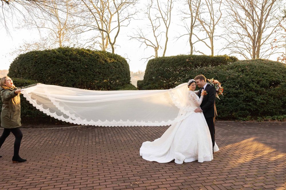 A couple in wedding attire poses together on a brick pathway during golden hour lighting.