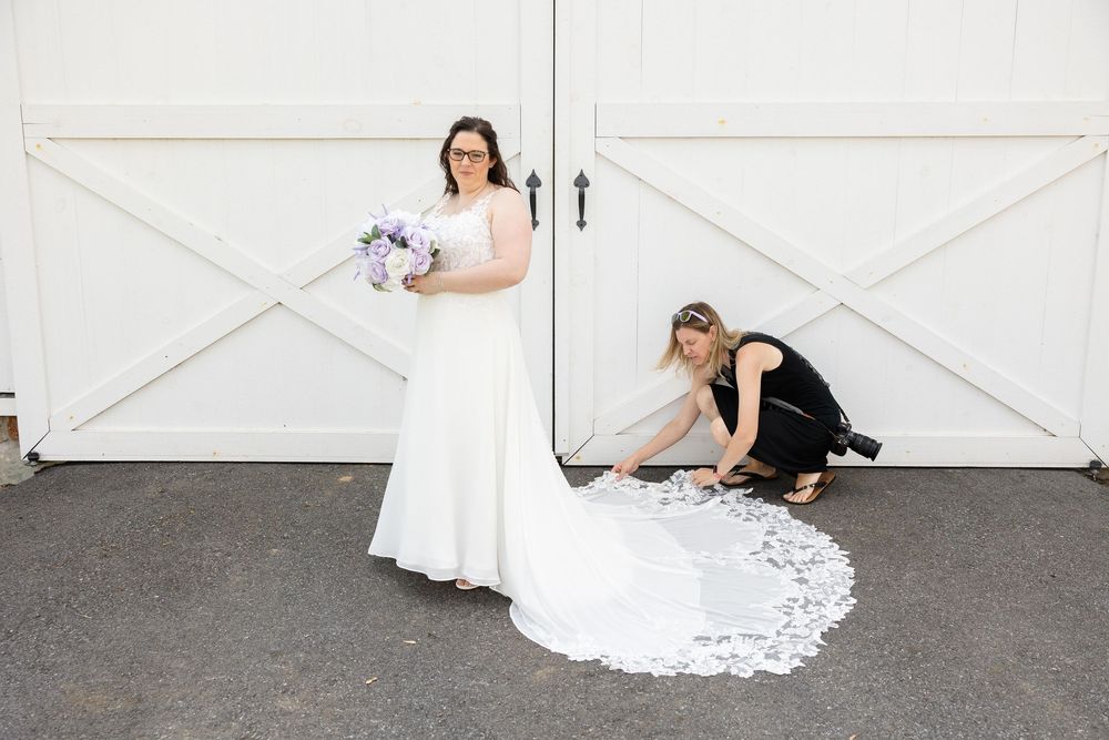 Two people in wedding dresses pose playfully in front of white barn doors.