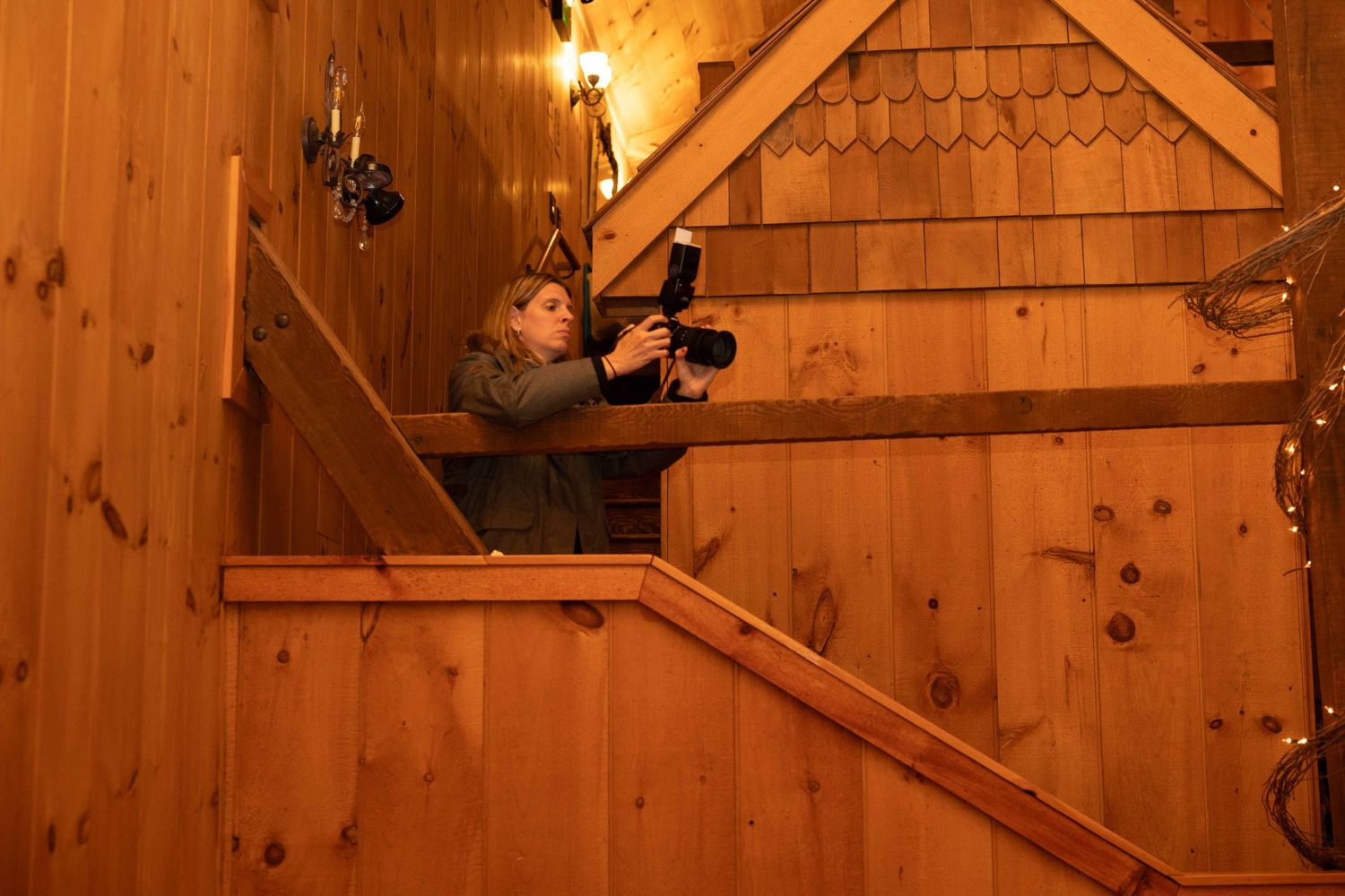 A figure wearing sunglasses and black clothing tilts their head back in a dramatic pose against a wooden backdrop.