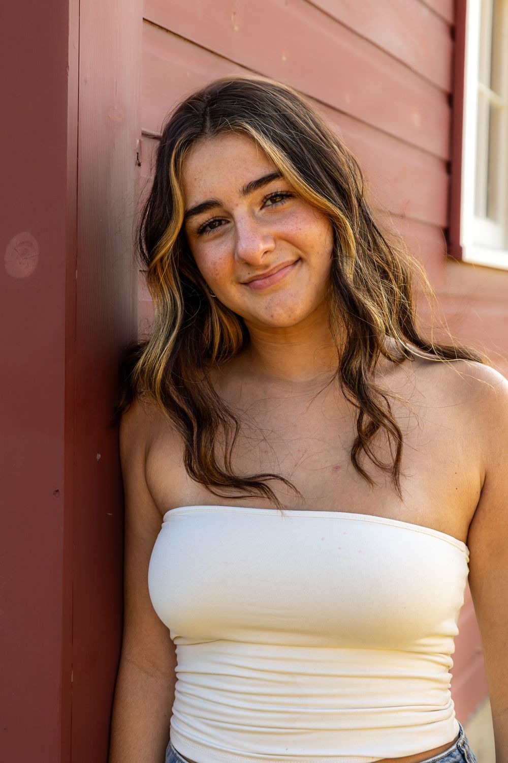 A person in a white strapless top poses against a red wall in a series of candid expressions.