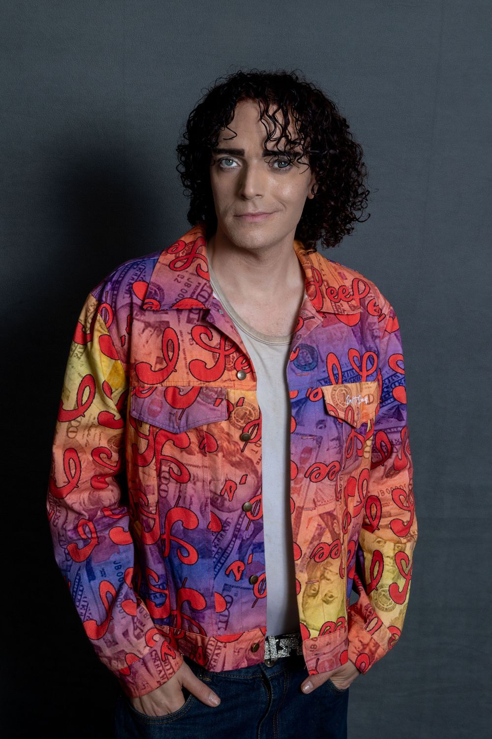 Portrait of someone wearing a vibrant colorful patterned jacket with curly dark hair against a gray background.