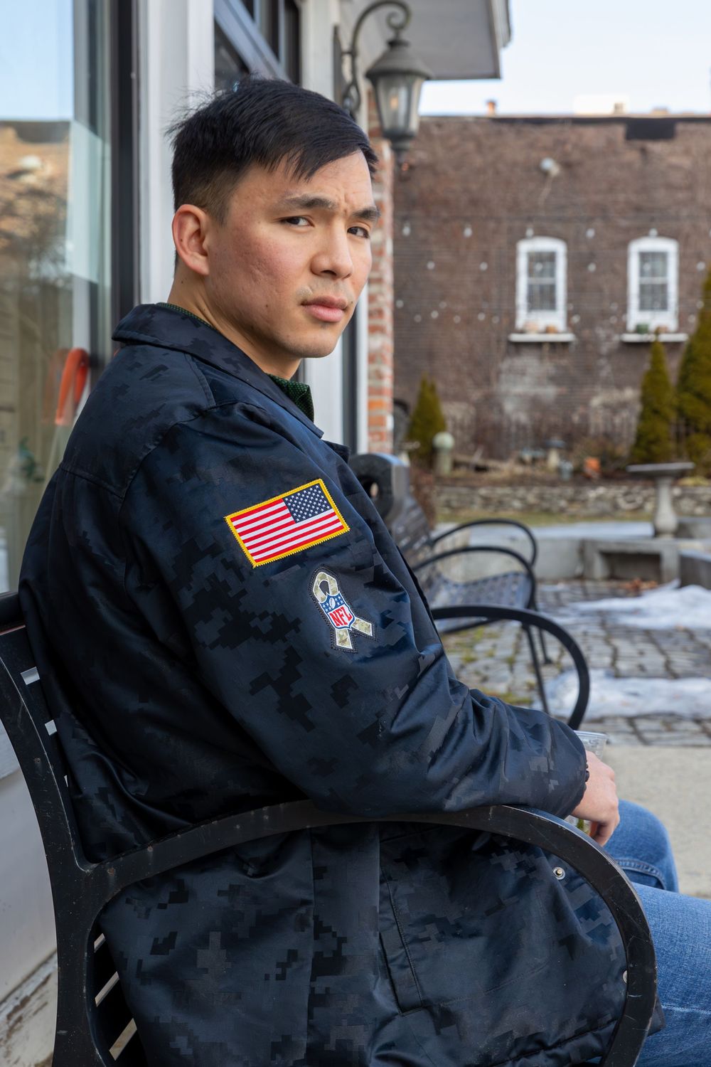 Person wearing a black jacket with American flag patch sits outdoors in winter setting.