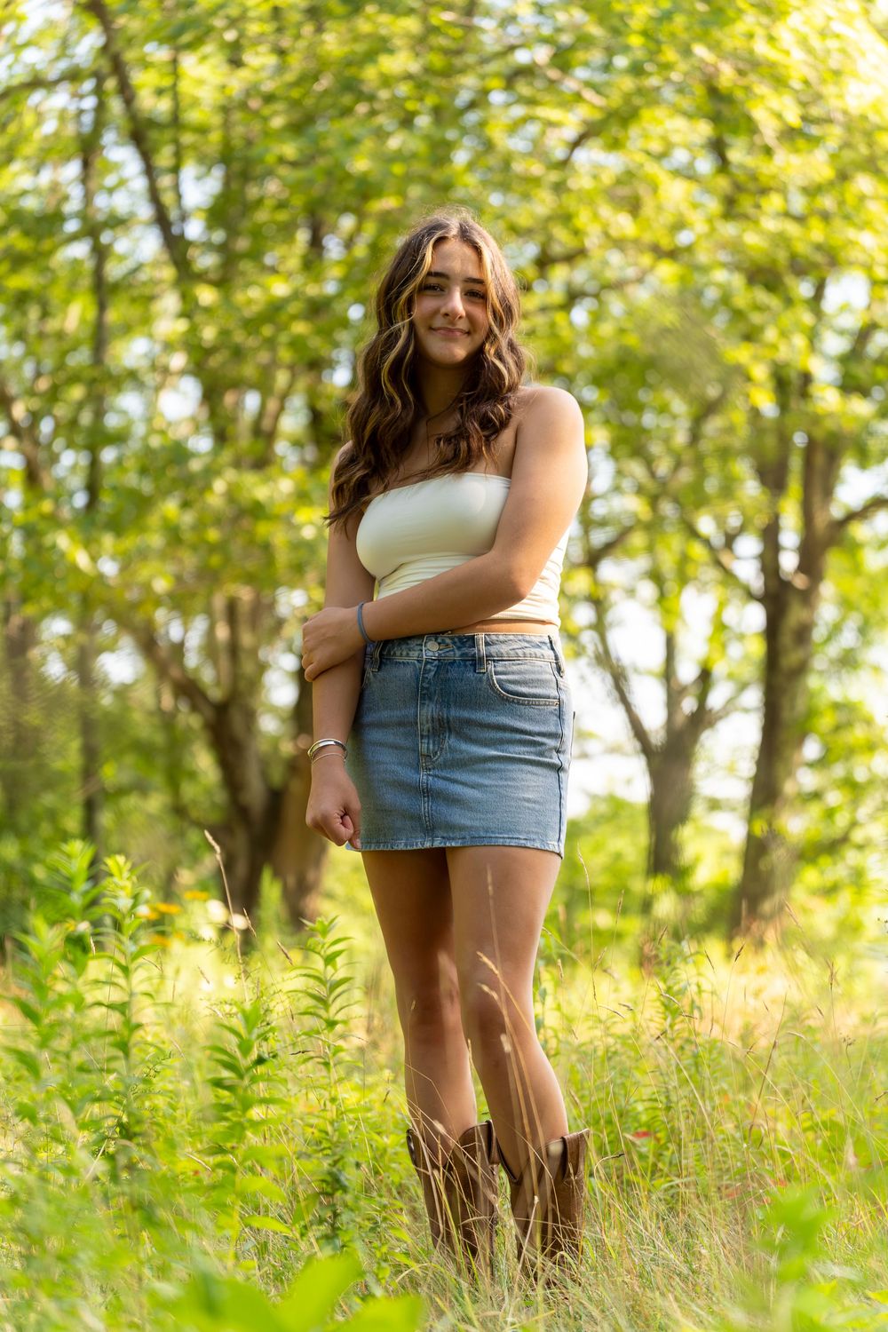 A person in denim shorts stands in a sunlit meadow with tall grass and trees creating a dreamy summer atmosphere.