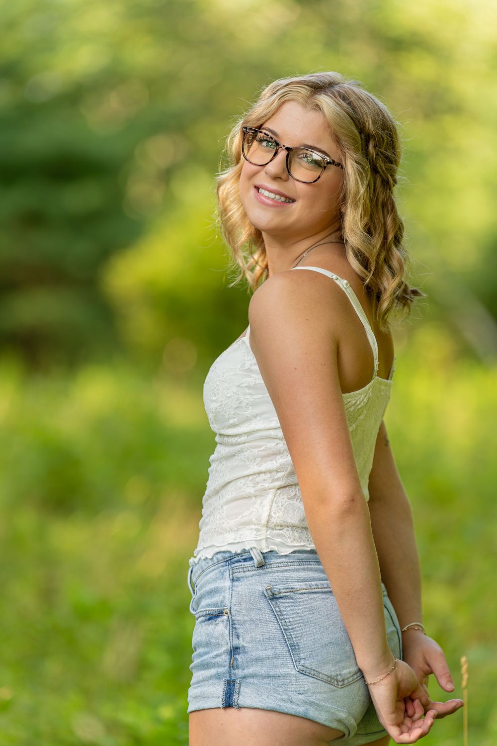 Outdoor portrait series showing a person in a white top and denim shorts against a soft green natural background.