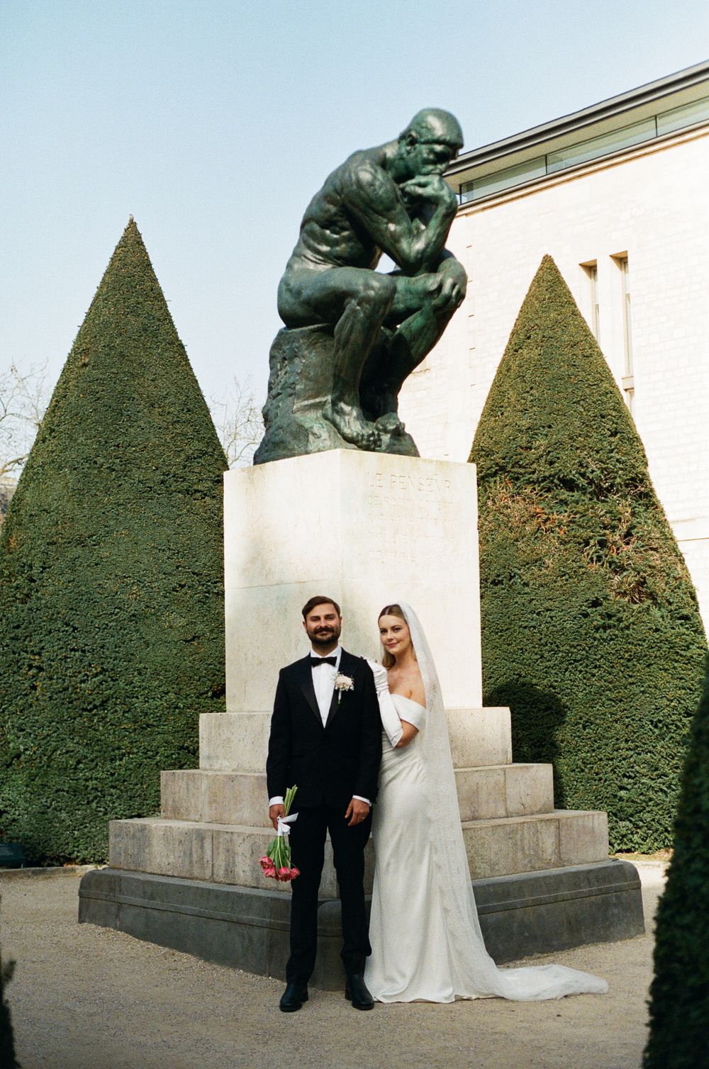 Bride and groom posing in front of Rodin's The Thinker sculpture at a garden wedding venue, paris wedding photos shot on film photography