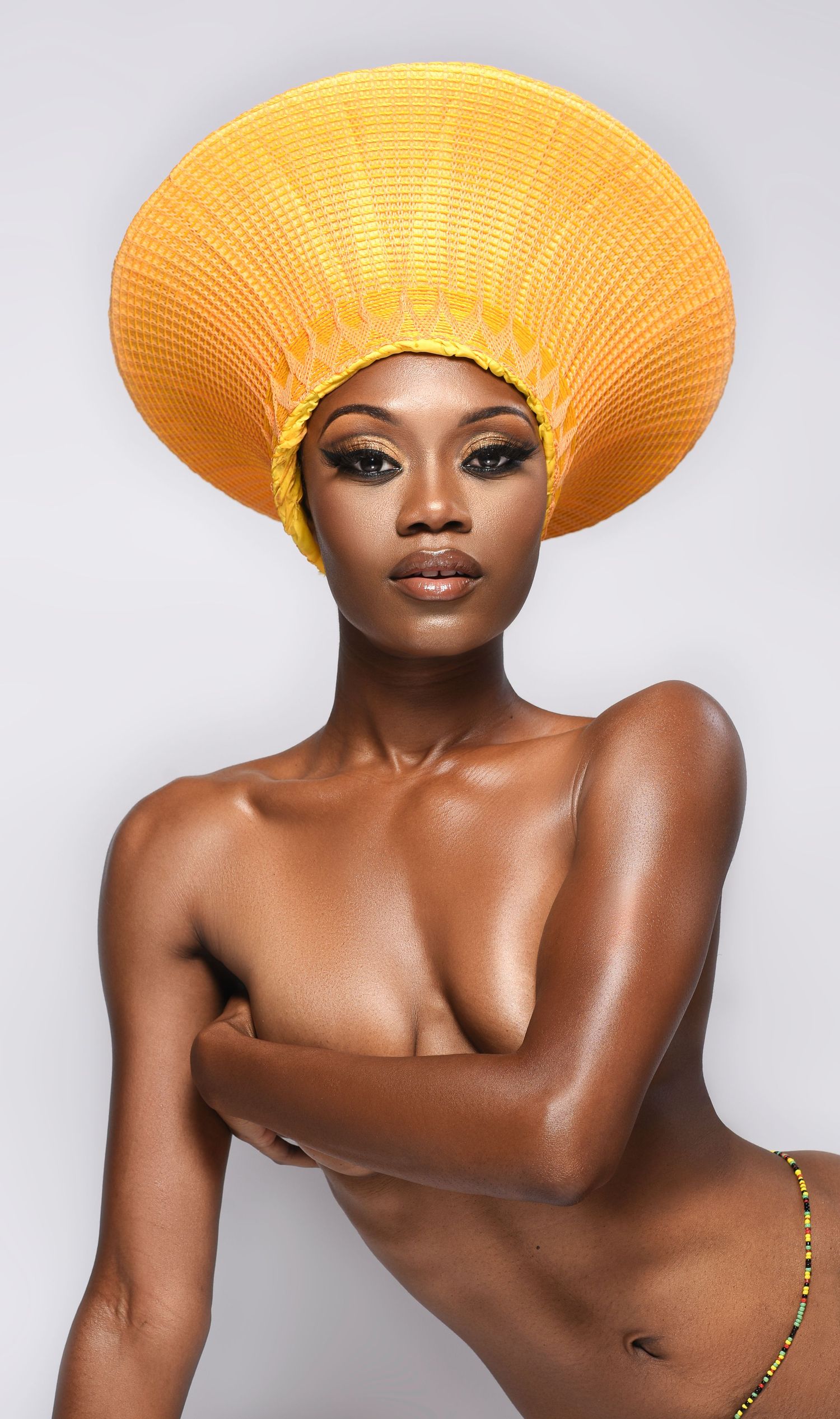 Artistic fashion portrait featuring a bright yellow sun hat against a light gray studio background.