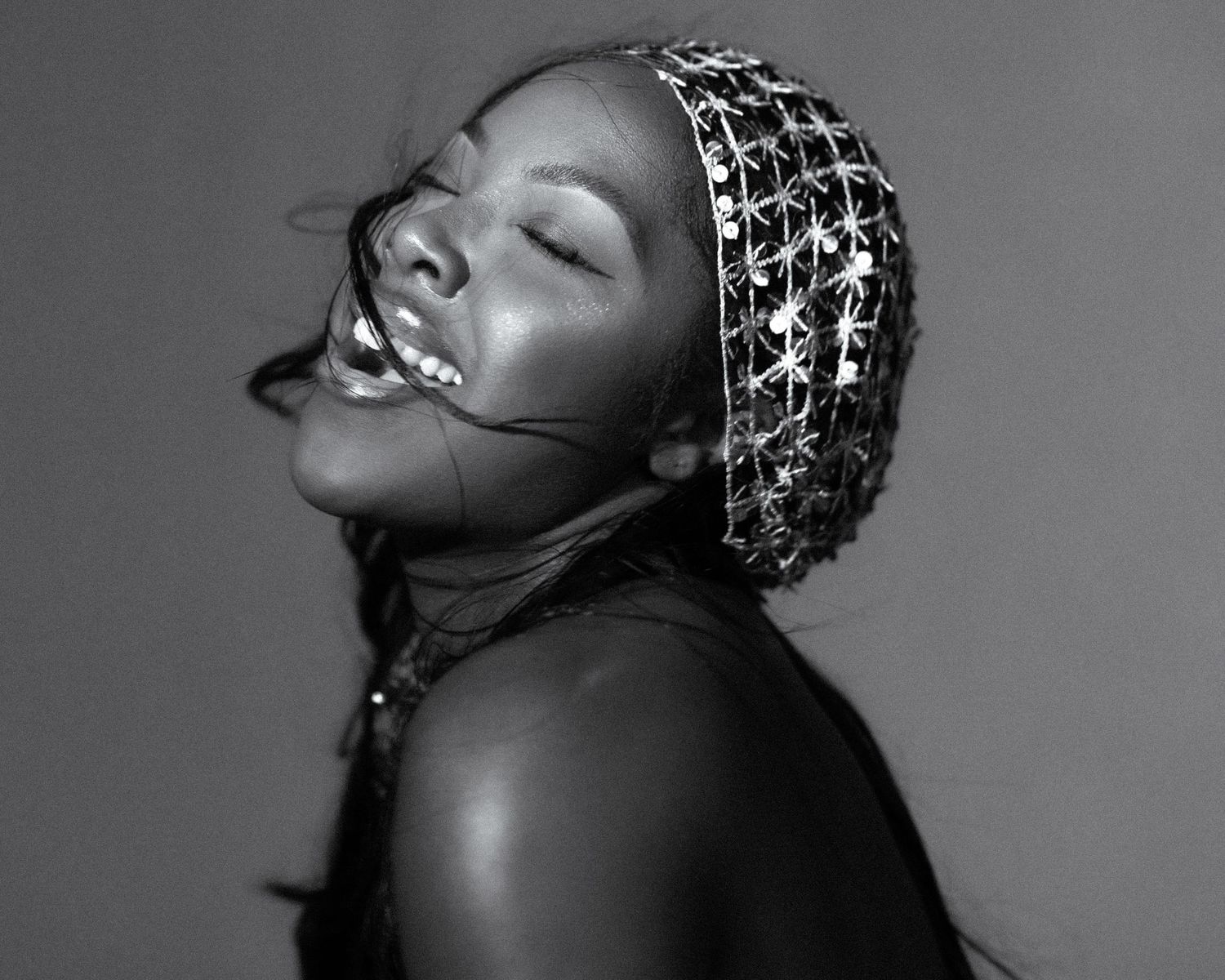 Black and white portrait of a woman laughing, wearing a decorative crystal headband, head tilted back.