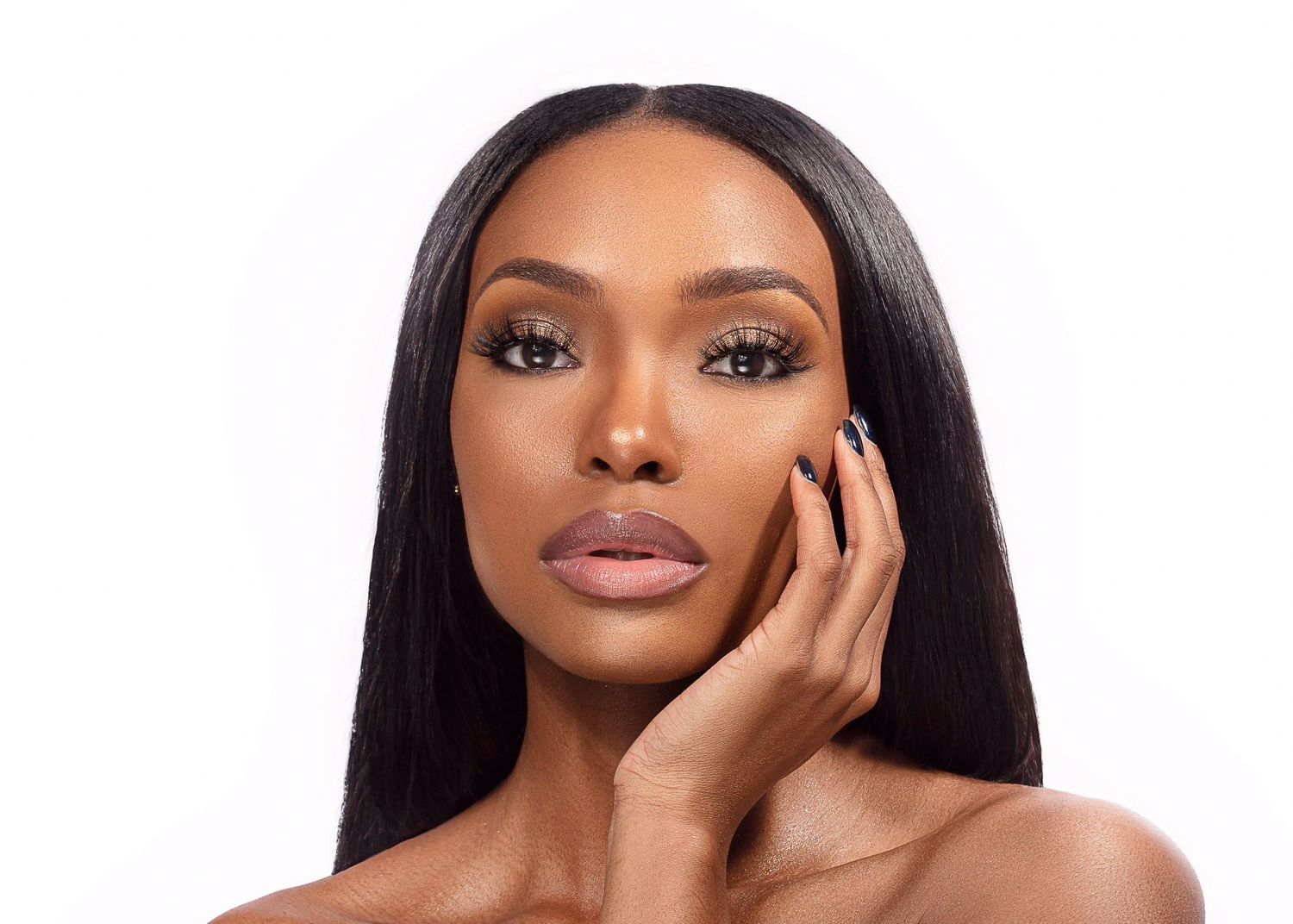 Beauty portrait of a woman with glowing skin, long straight black hair and neutral makeup against white background.