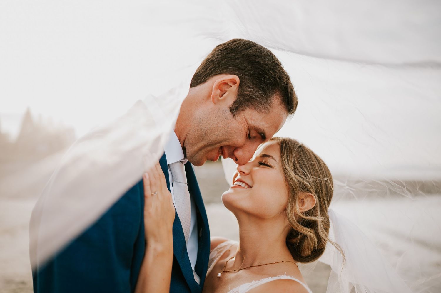 Wedding photography of couple on Williams Beach, groom and bride during golden hour under wedding veil smiling with eyes closed