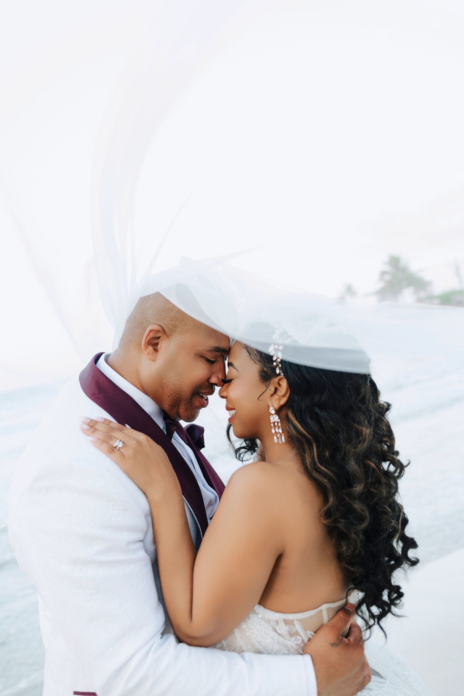 A tender moment shared between newlyweds as a veil flows in the breeze, capturing their romantic embrace outdoors.