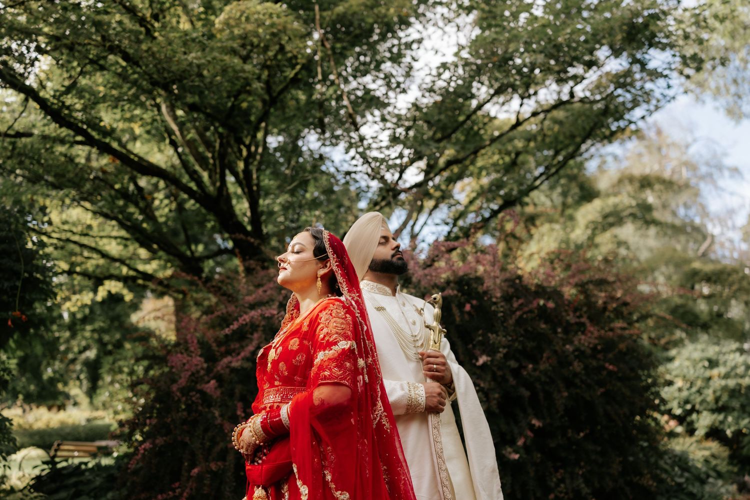 A couple in traditional wedding attire sharing a joyful moment in a garden setting.