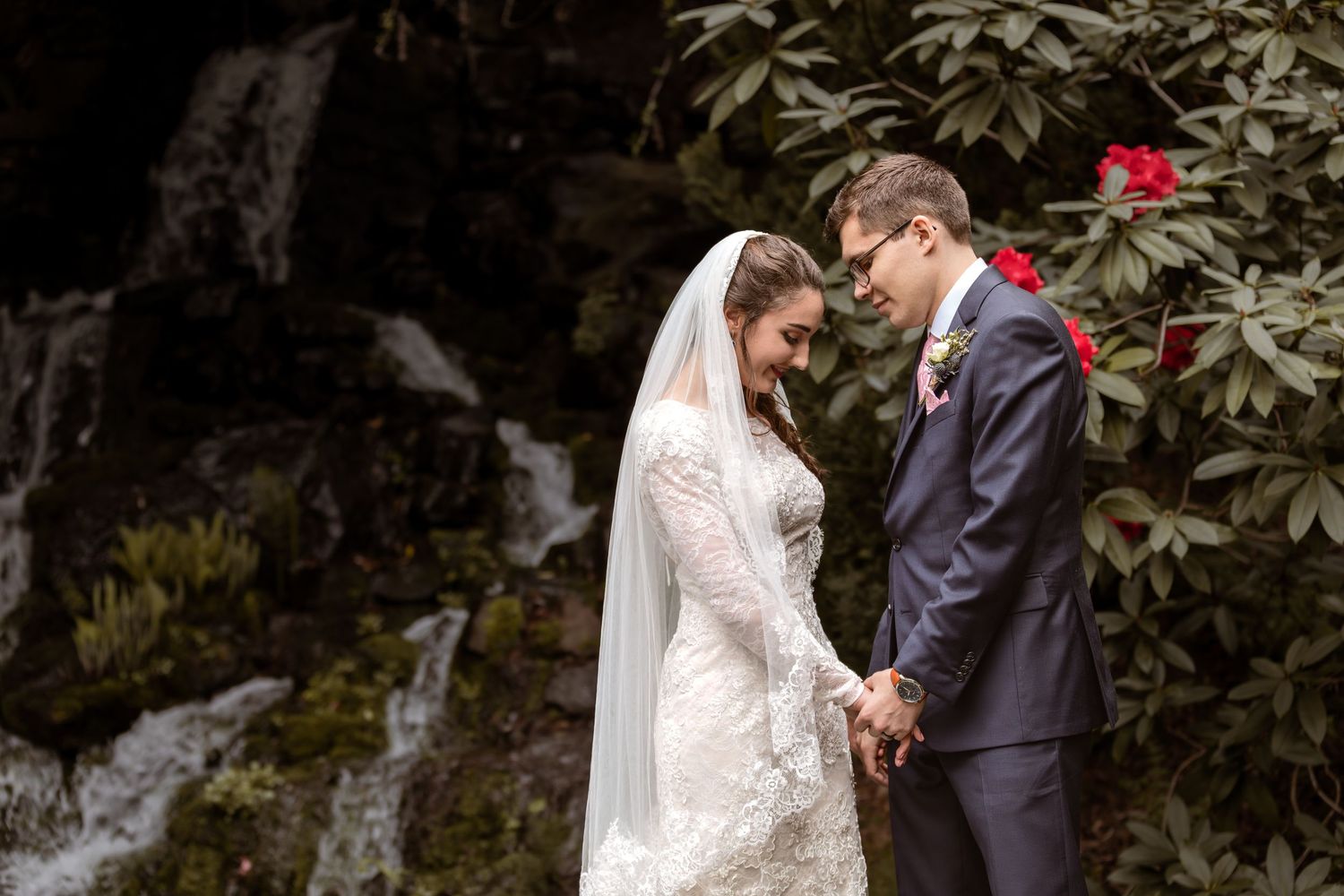 A romantic wedding couple embraces in a lush garden setting with cascading greenery and natural light.