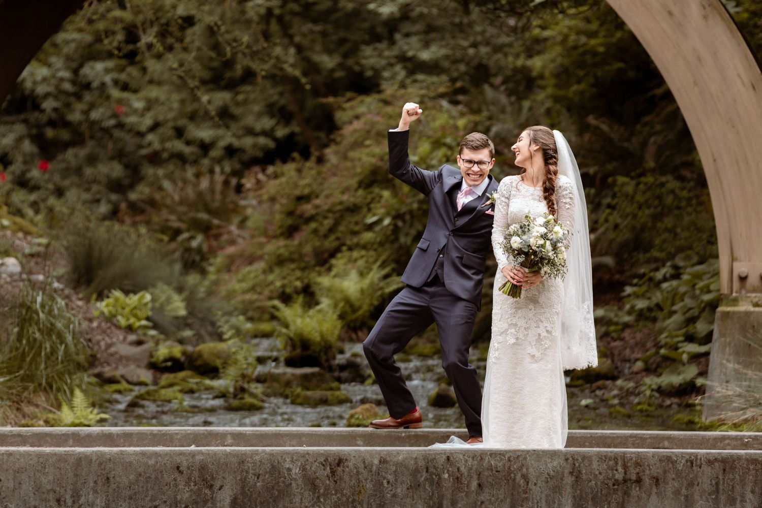 Whimsical wedding photo of newlyweds posing playfully under a garden arch.