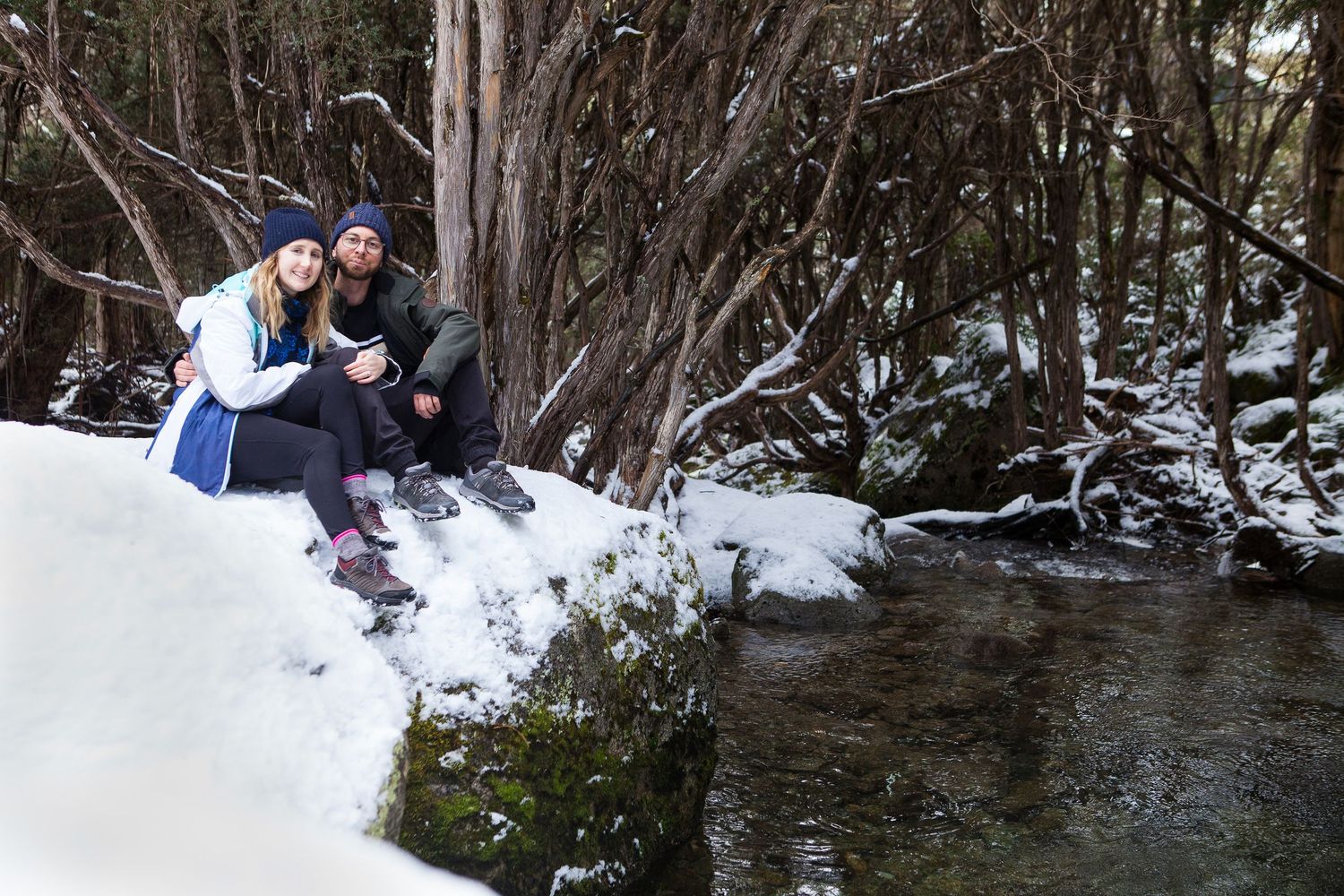 A couple embrace during proposal photoshoot sitting on a snowy rock alongside the Thredbo
