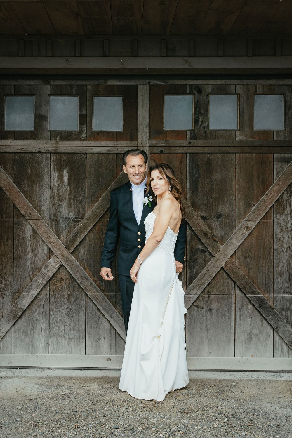 A couple in wedding attire poses against a rustic wooden barn wall in a series of romantic shots.
