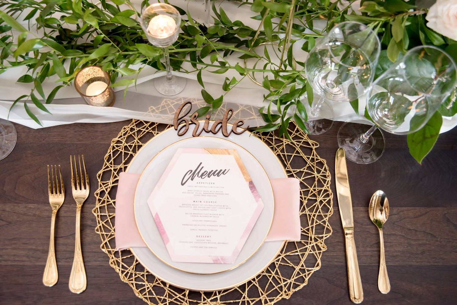 Photo of a Wedding table place setting showing a wire gold charger, gold cutlery, laser cut wood name and menu.