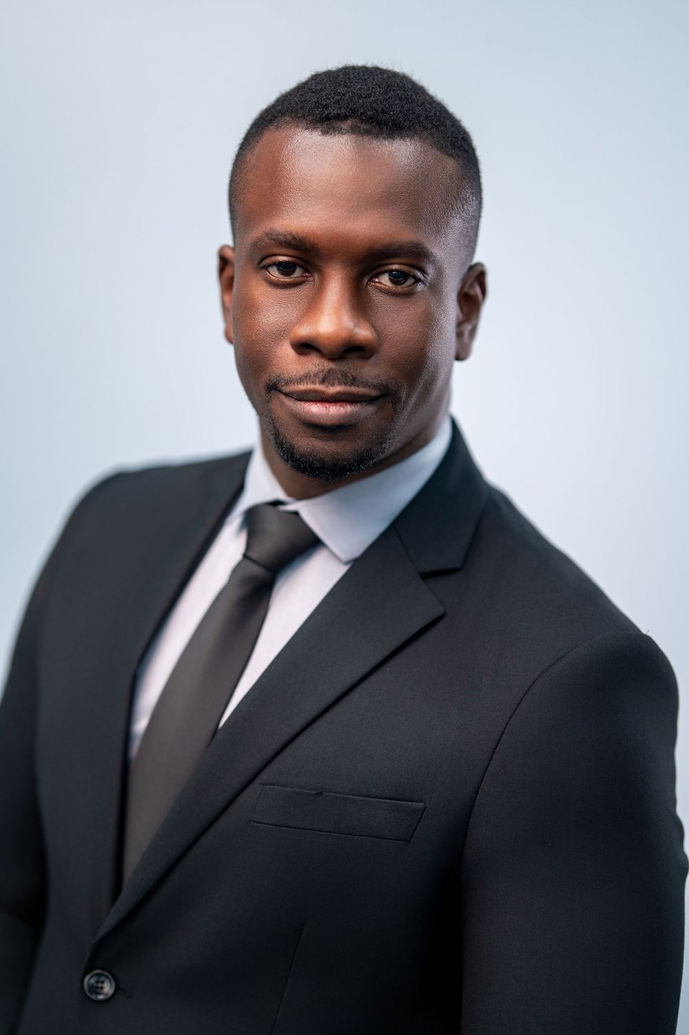 Professional headshot series showing different angles of a person in a black suit and tie against a light background.
