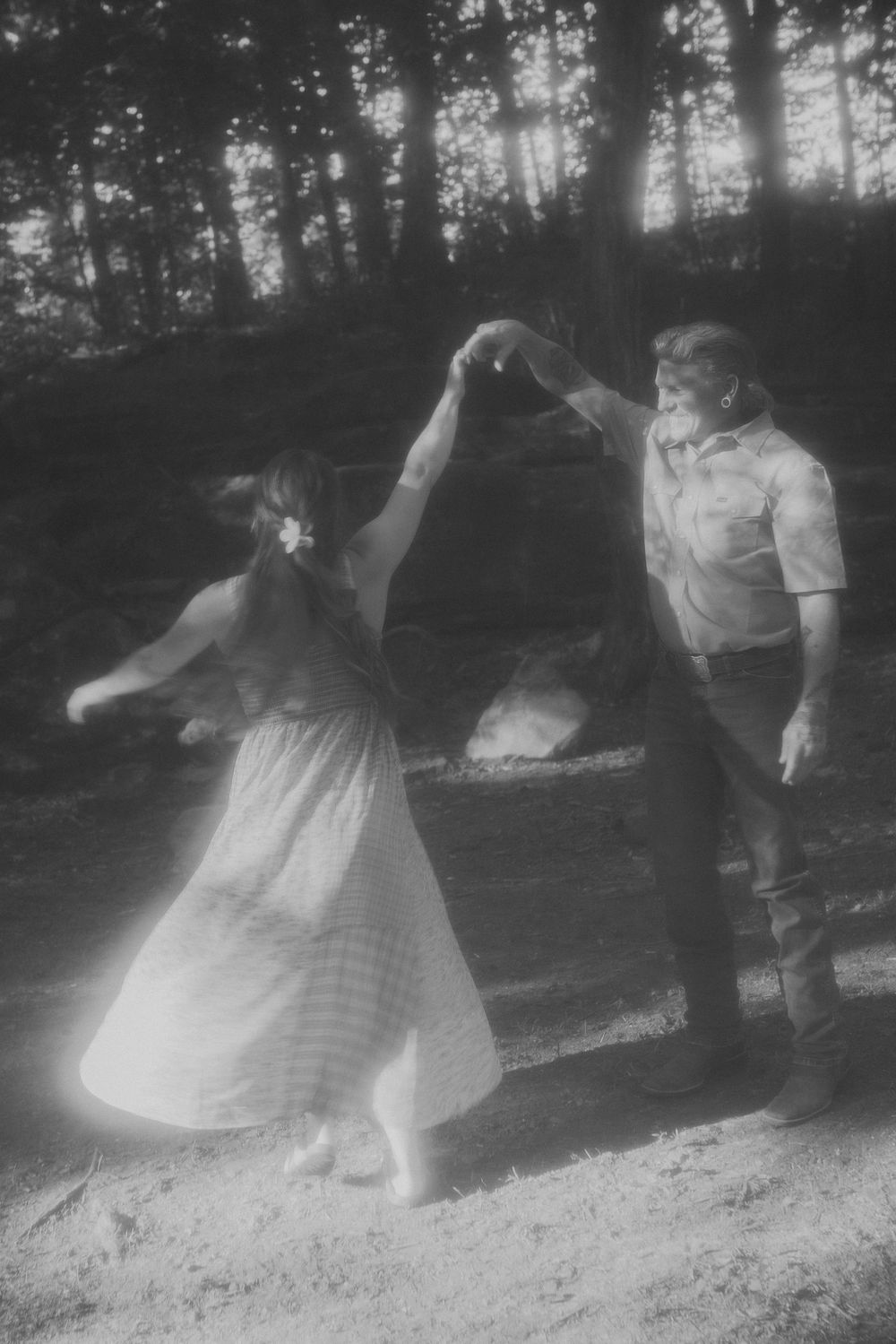 Black and white photo of a couple dancing together in a sunlit forest clearing.