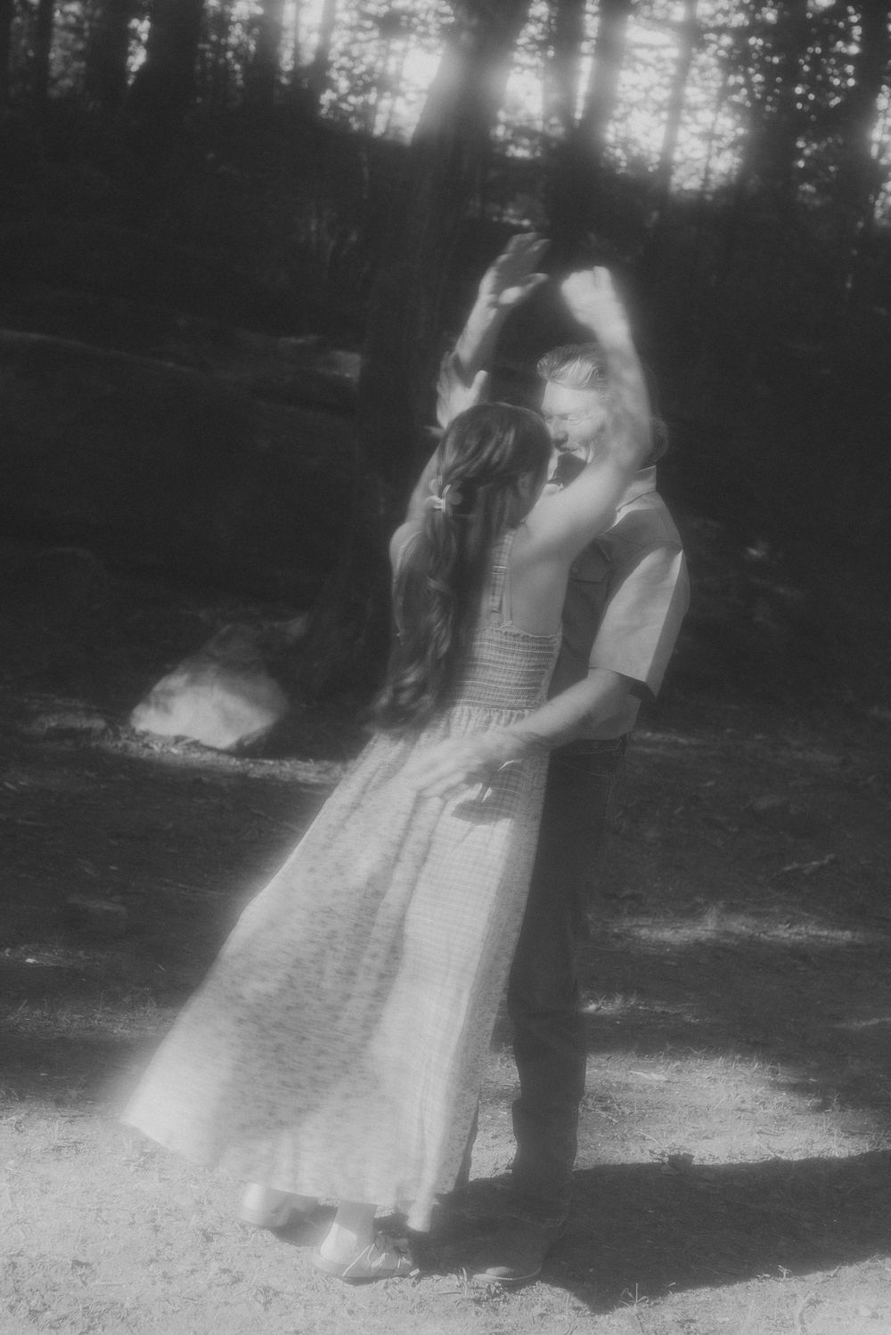 A romantic black and white photo of a couple slow dancing in a forest with dreamy soft focus.