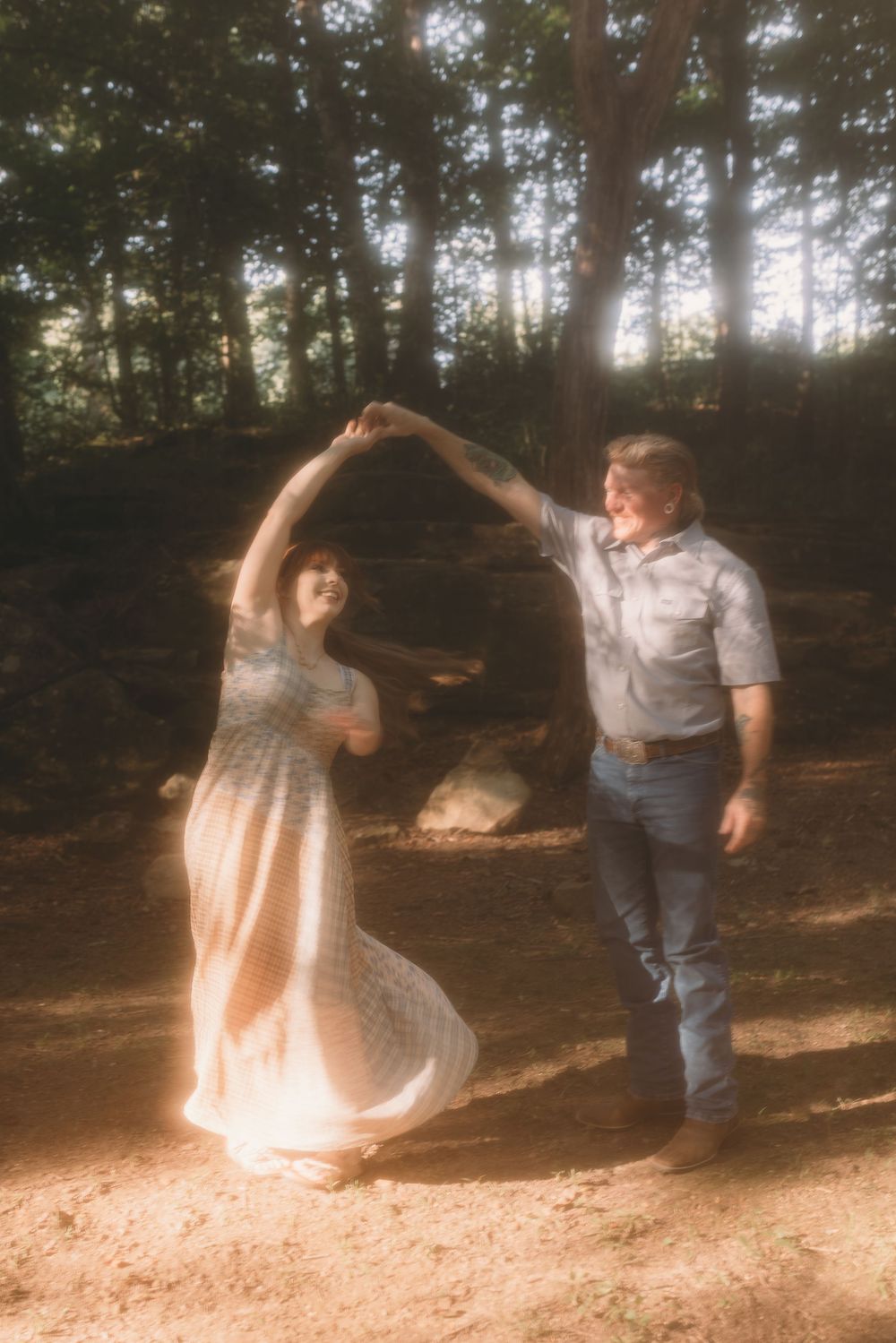 A couple dances together in a sunlit forest clearing, the woman wearing a flowing white dress.