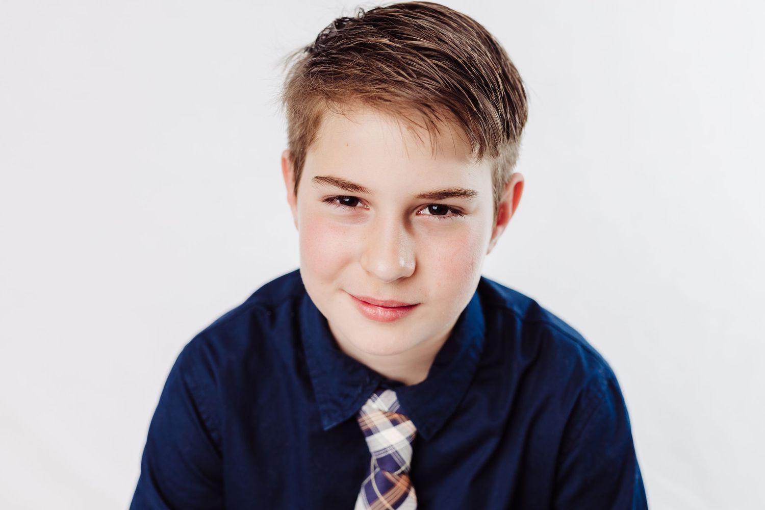Young student poses in navy blazer and tie against white background for professional school photo.