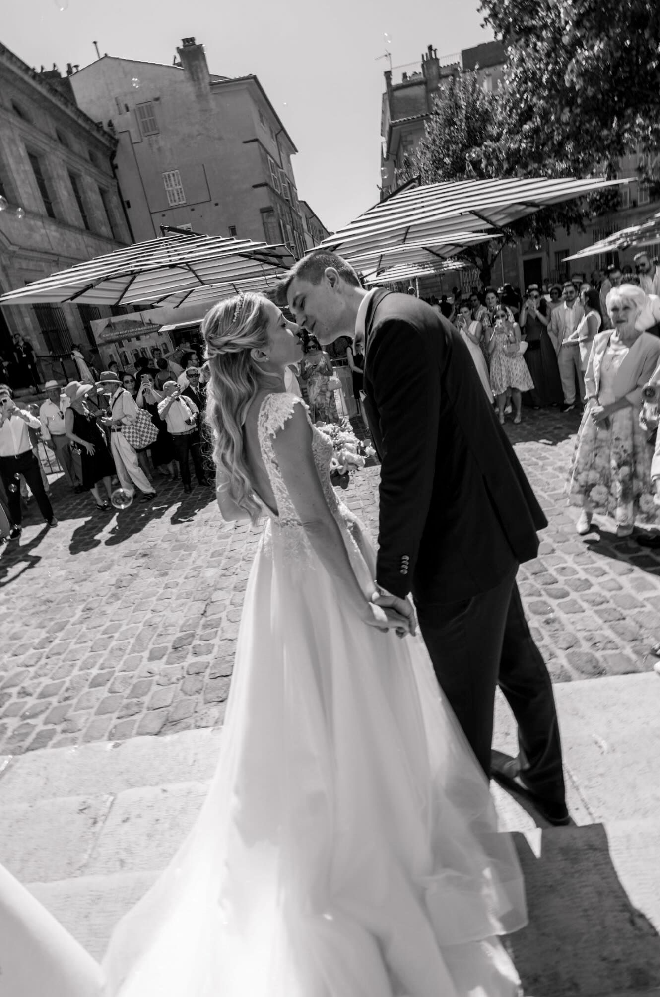 A couple dancing together at a wedding celebration on cobblestone streets with guests watching in the background.