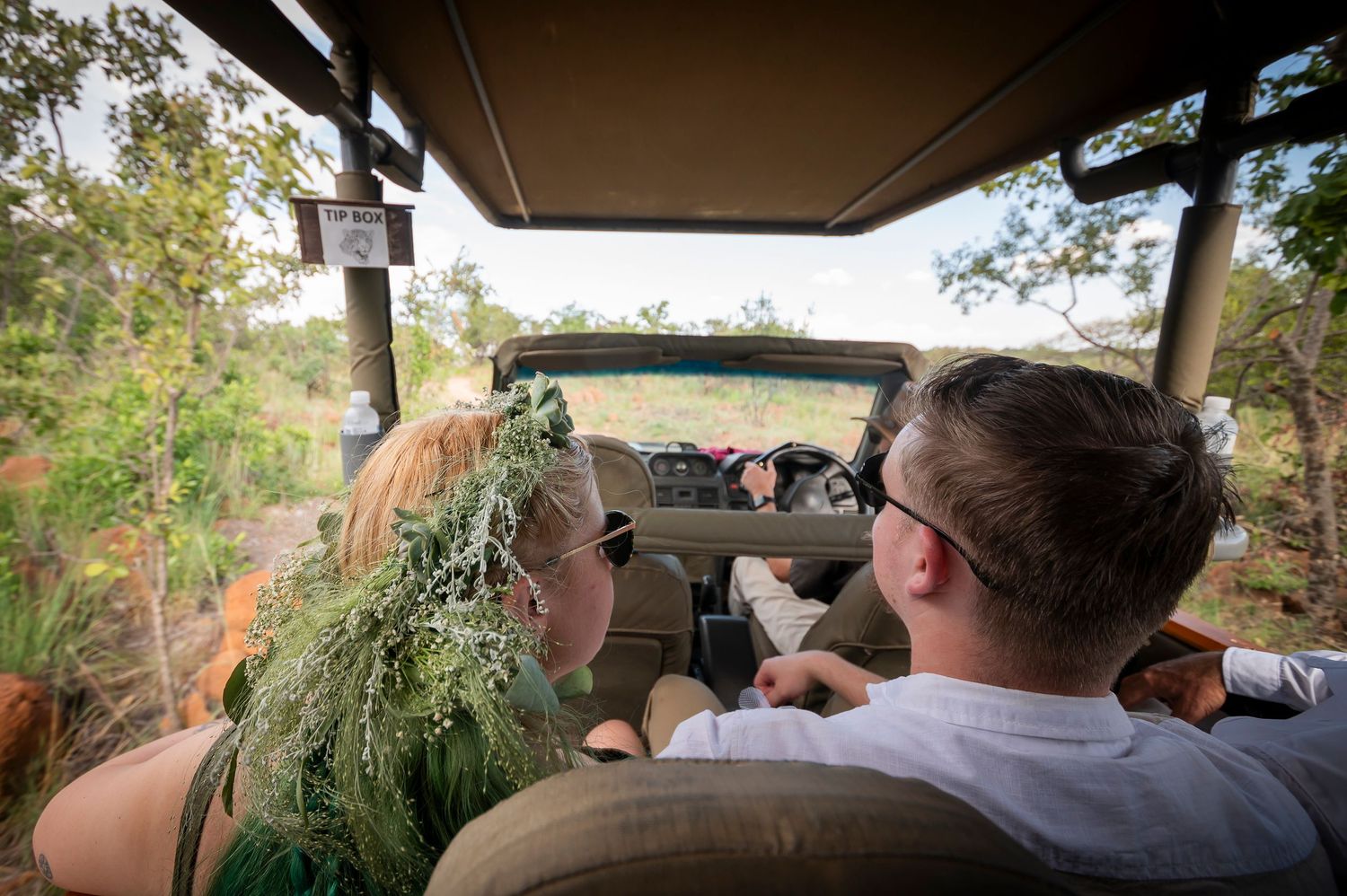 Couple on a safari game drive through lush African bush in an open vehicle.