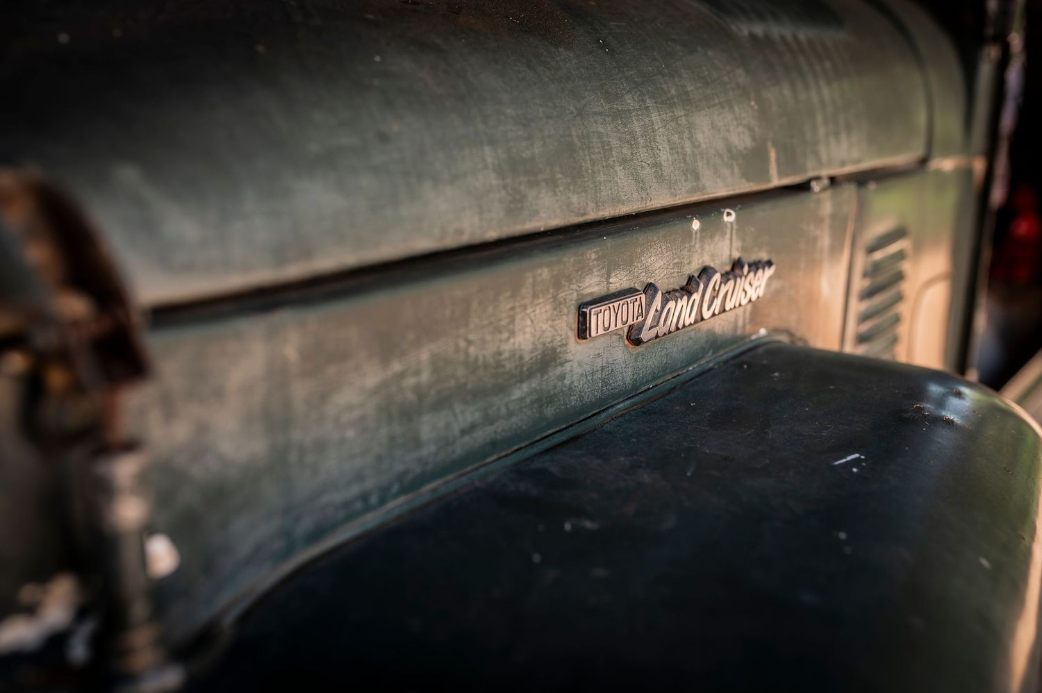 Close-up of a vintage Toyota Land Cruiser emblem on a weathered, patina-covered green vehicle body.