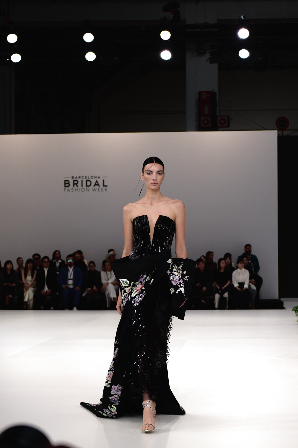 Dramatic black evening gowns with floral embellishments presented on a pristine white catwalk.