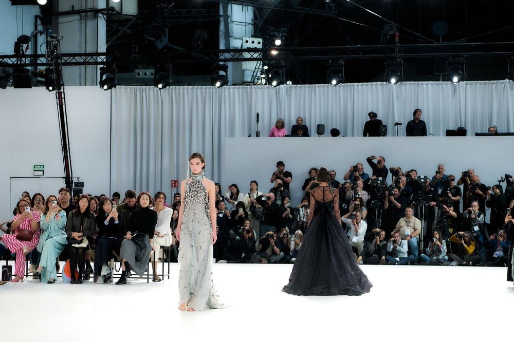 Wide shot of fashion runway show with models and audience in modern venue.