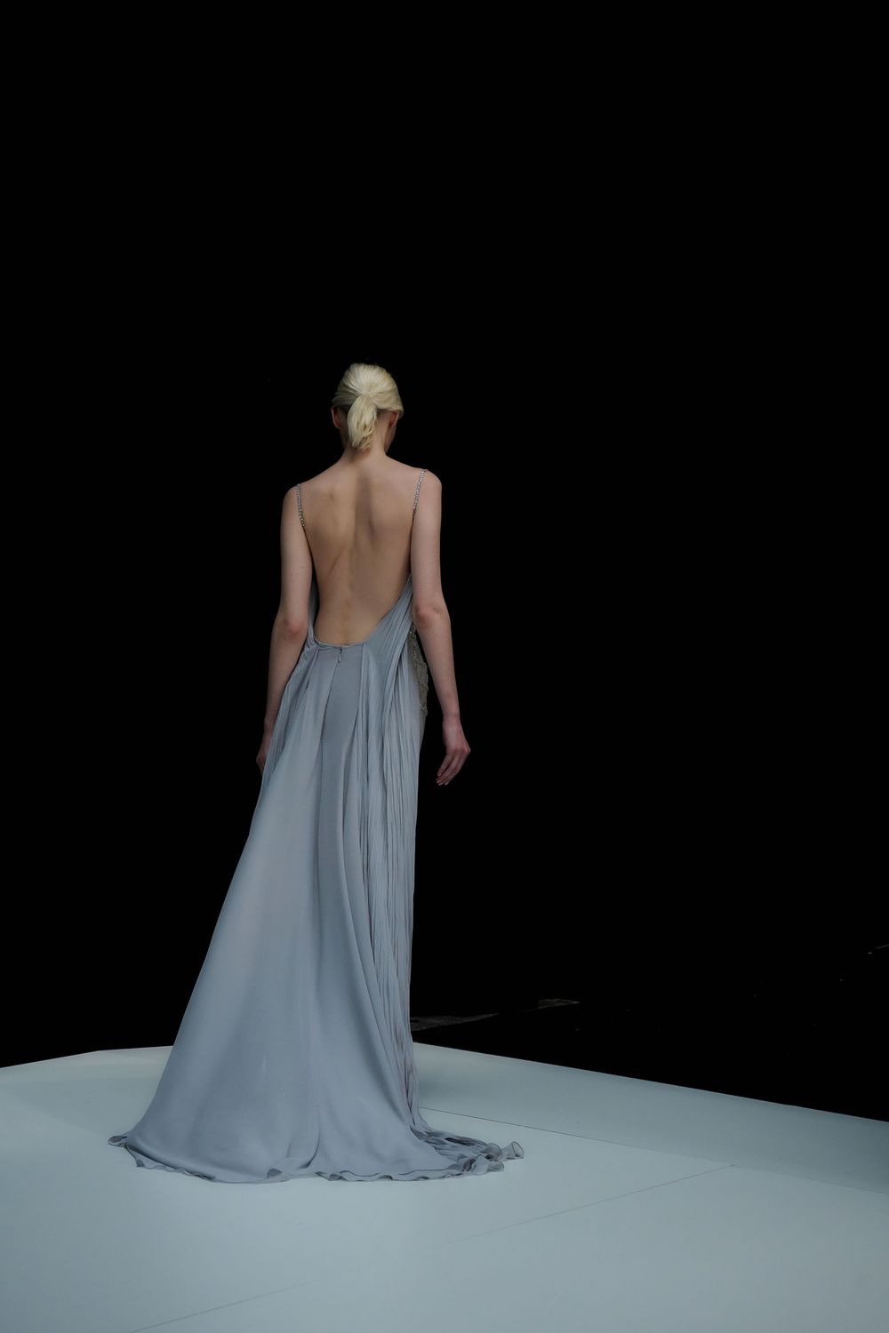 Dramatic backless grey gown photographed against dark background on white runway.