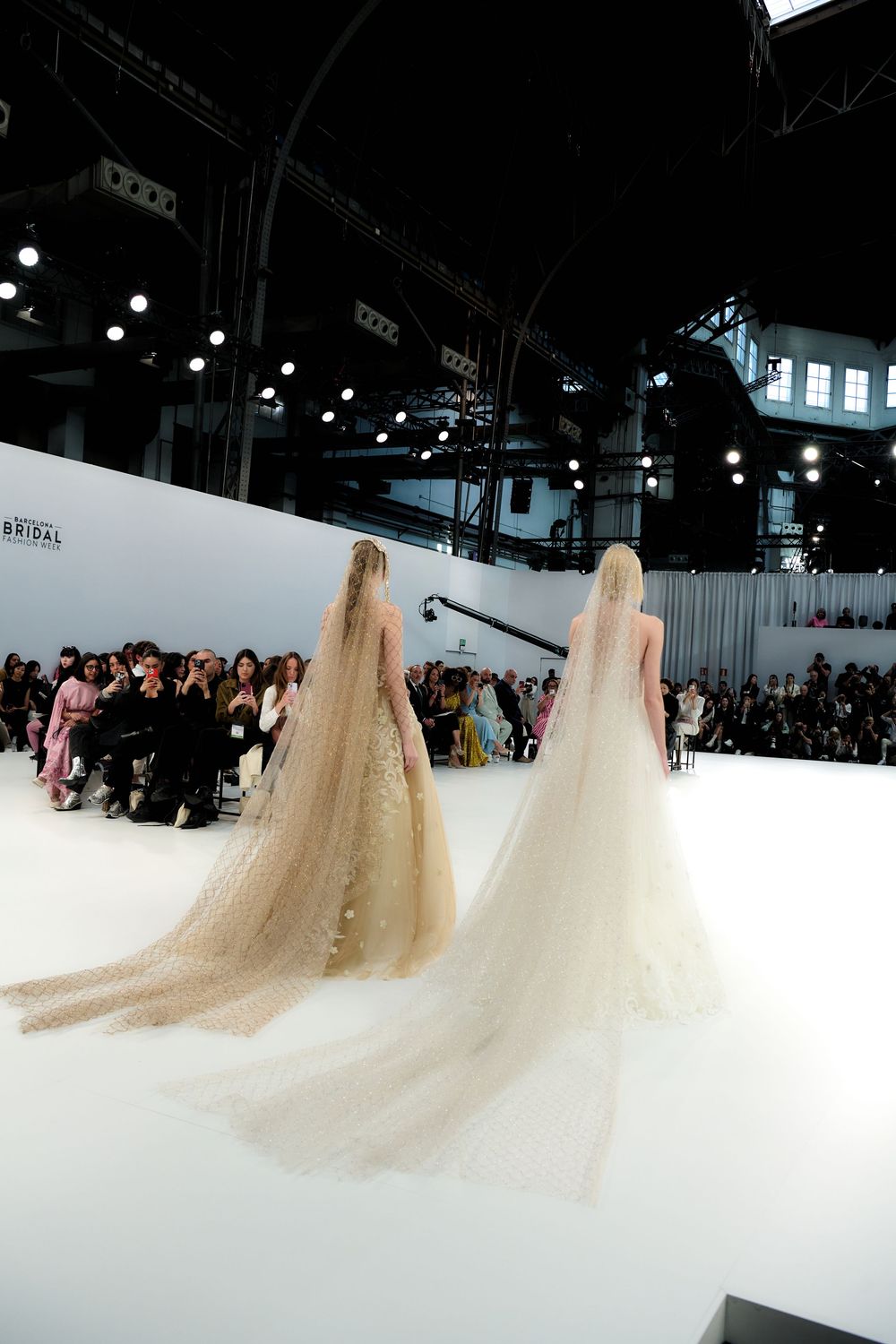 Multiple bridal gowns create an ethereal procession of flowing trains on a white catwalk.
