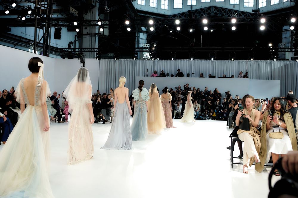Wide view of a bridal fashion show featuring multiple wedding gowns on an illuminated runway.