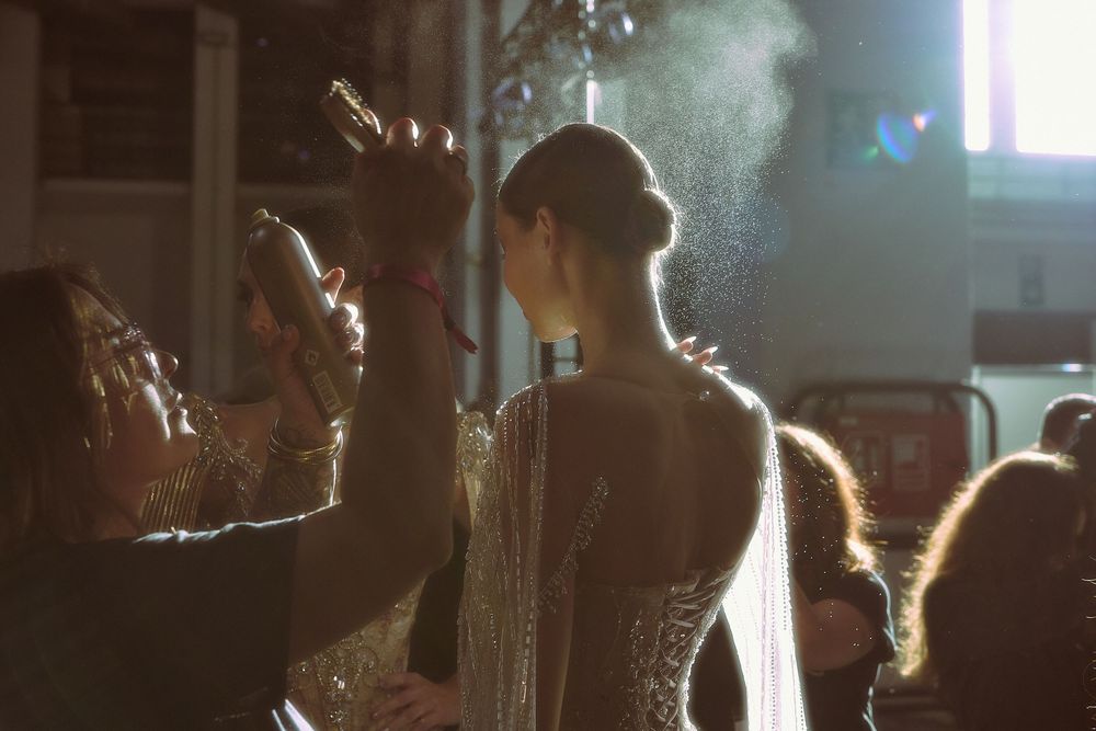 Ethereal lighting creates moody silhouettes of models walking a dimly lit fashion runway.