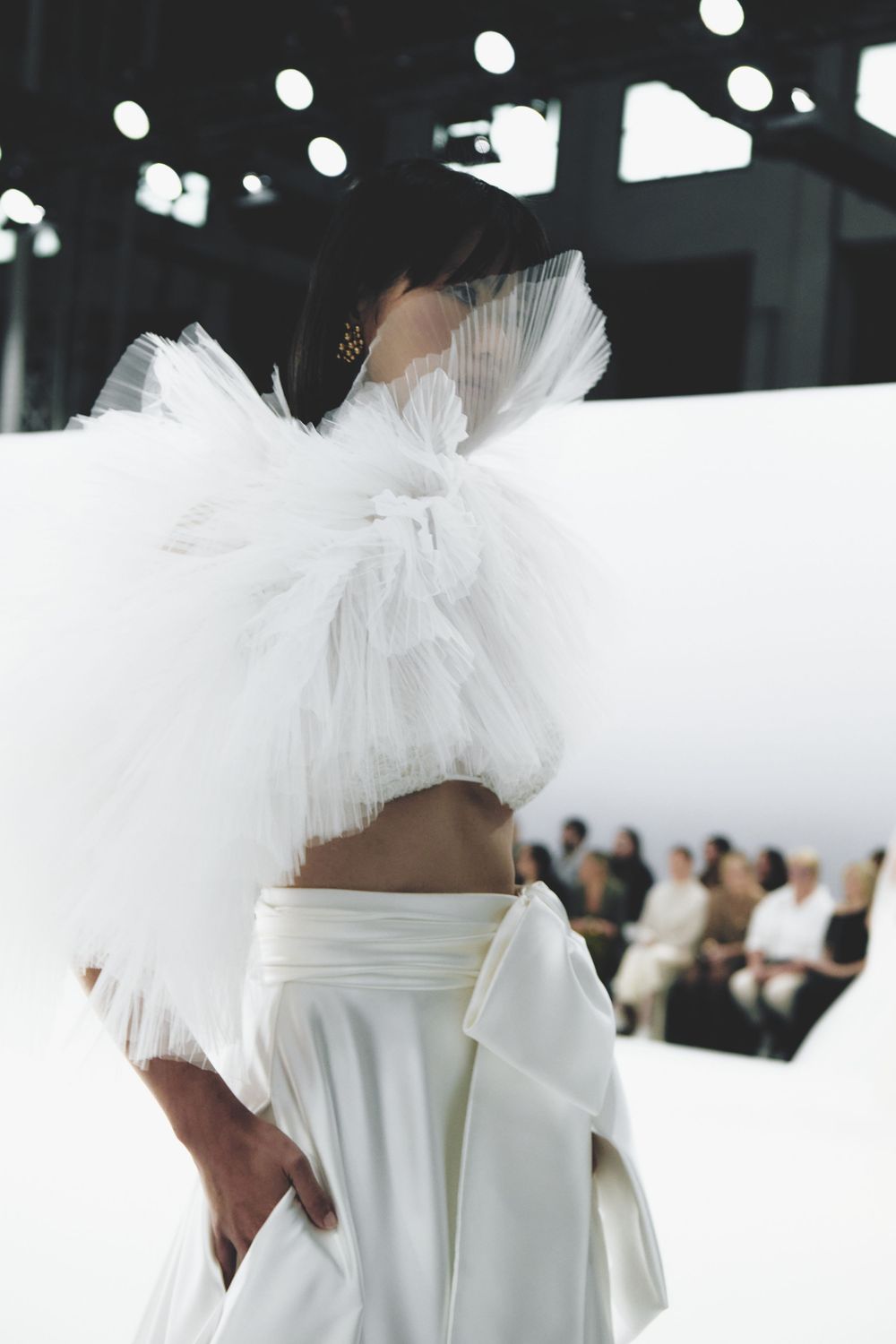 Models showcase ethereal white tulle gowns on a minimalist runway at a bridal fashion show.
